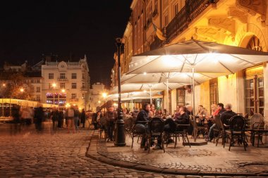 Lviv, Ukrayna - 19 Nisan 2019: Gece şehrinin eski sokaklarında sokak kafe. Eski şehir pazar meydanında Lviv şehir ışıklı gece insanlar kafede masalarda oturan. uzun pozlama