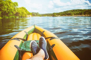 İnsan nehirdeki sarı teknede dinlenir. Ayaklarında yakın çekim ayakkabılar var. Teknede çapraz ayakları nabak. Pov