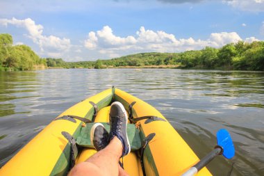 İnsan nehirdeki sarı teknede dinlenir. Ayaklarında yakın çekim ayakkabılar var. Teknede çapraz ayakları nabak. Pov