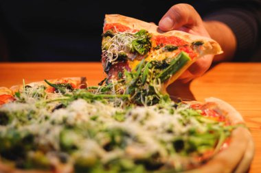 kadın Mozzarella peyniri, Domates, biber, zeytin, Baharat ve Taze Fesleğen ile dilimlenmiş Pizza bir dilim alır. İtalyan pizzası. Ahşap masa arka planda vejetaryen pizza