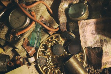 Masada farklı antika öğeler: bronz takı, eski para, retro manometre, büyüteç, cam şişe, gümüş. Antika koleksiyonundan vintage arka plan. Yakın çekim seçili odak