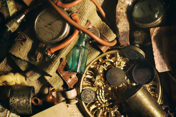 Различные антикварные предметы на столе: бронзовые украшения, старые деньги, ретро-манометр, лупа, стеклянная бутылка, столовое серебро. Винтажное происхождение из коллекции антиквариата. Выбранный крупный план
