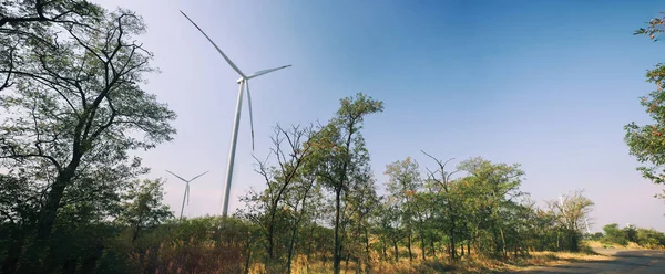 Wind turbine on field. Empty road in foreground, blue sky  on background. Alternative energy source, production and power generation. Ecology and freedom concept. Panorama. — Stock Photo, Image