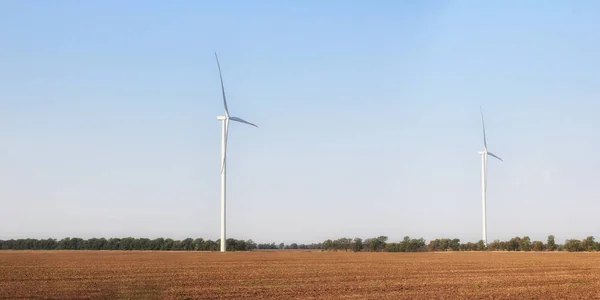 Vindkraftverk på fältet. Tomt fält i förgrunden, blå himmel på bakgrunden. Alternativ energikälla, produktion och kraftproduktion. Ekologi och frihets koncept. Panorama. — Stockfoto