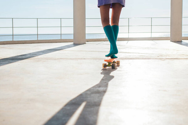 Close-up of female young girl legs in green socks  standing on a orange  plastic skateboard. Summer sports activities for teens, active kids lifestyle. socks advertising concept