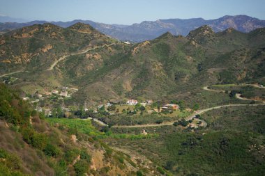 Açık mavi gökyüzünün altındaki ağaçlı yeşil tepelerin güzel bir görüntüsü.