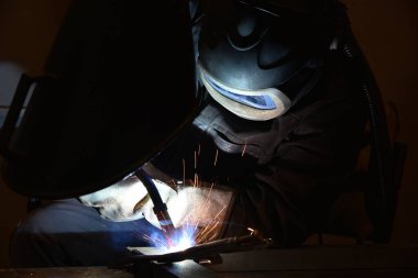 Metal ve kıvılcımlar üreten koruyucu maskeli bir işçi. Kaynakçı metali kaynaklıyor..