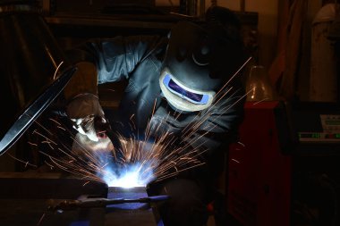 Metal ve kıvılcımlar üreten koruyucu maskeli bir işçi. Kaynakçı metali kaynaklıyor..