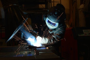 Metal ve kıvılcımlar üreten koruyucu maskeli bir işçi. Kaynakçı metali kaynaklıyor..