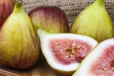 Taze incir dilimlenmiş, arka planda incir var, ahşap bir yüzeyde. Tahta tabakta incir meyveleri.