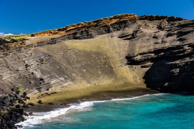 Hawaii 'nin Big Island South Point yakınında yeşil kum plaj (papakolea). Eski yanardağ koni dik eğim plajın arkasında; mavi-yeşil okyanus & derin mavi gökyüzü. 