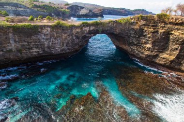 Endonezya 'nın Nusa Penida adasındaki Broken Beach. Ön planda kayalar ve berrak turkuaz su ile göl; uzakta engebeli kıyı şeridi. 