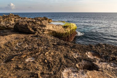 Nusa Lembongan, Bali, Endonezya 'daki Devil' s Tear 'da Rocky kıyı şeridi. Önünde gelgit havuzu olan kayalık bir sahil. Arkaplanda kıyı şeridi, okyanus, gökyüzü & bulutları. 