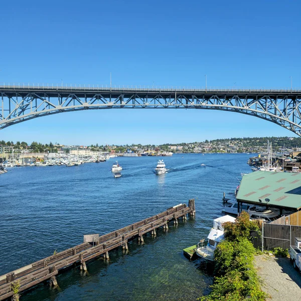 Seattle, Washington 'da parlak bir yaz günü, ikonik Aurora Köprüsü George Washington Memorial Köprüsü' nün yer aldığı Lake Union boyunca uzanan bir köprü. Tekneler ve yatlar çelik yapının altında huzur içinde yüzüyor. Şehir silüeti ve mahalleleriyle birlikte.