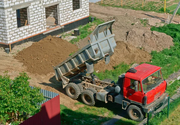 the truck and building of the house from a white brick, the dump truck brought sand on building, the dump truck near the house under construction