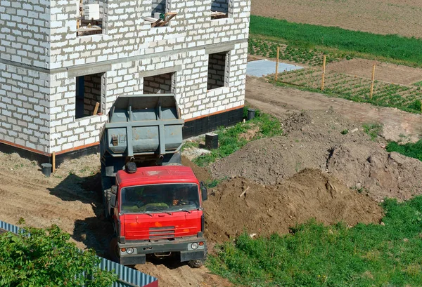 the truck and building of the house from a white brick, the dump truck brought sand on building, the dump truck near the house under construction
