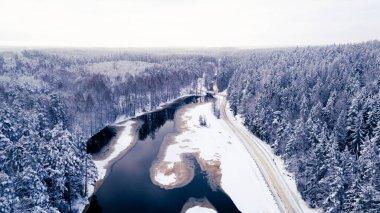 Dolambaçlı bir nehir ve yolu olan karlı bir ormanın havadan görünüşü.