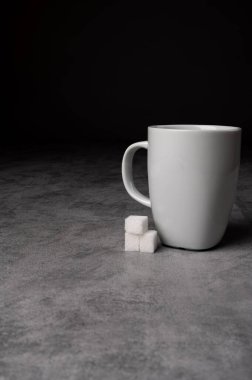 Beyaz seramik kahve fincanının gri taş bir yüzeye koyu arkaplana yerleştirilmiş şeker küplü minimalist stüdyo görüntüsü. Sıcak içecekler, kahvaltı, kafein veya yaşam tarzı modelleri için kavramsal görüntü.