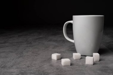 Beyaz seramik kahve fincanının gri taş bir yüzeye koyu arkaplana yerleştirilmiş şeker küplü minimalist stüdyo görüntüsü. Sıcak içecekler, kahvaltı, kafein veya yaşam tarzı modelleri için kavramsal görüntü.