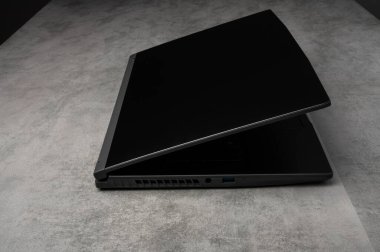 Modern siyah dizüstü bilgisayar gri bir yüzeyde yarı açık. Teknoloji, ofis işi, dijital iletişim ve taşınabilir bilgisayar temaları için mükemmel.