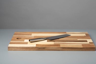 Çizgili ahşap bir kesme tahtasına yerleştirilmiş mutfak bıçağının yukarıdan görünüşü. Fotokopi alanı olan yemek tarifleri, yemek pişirme ve mutfak tasarımı için temiz gıda hazırlama geçmişi.