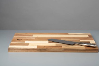 Çizgili ahşap bir kesme tahtasına yerleştirilmiş mutfak bıçağının yukarıdan görünüşü. Fotokopi alanı olan yemek tarifleri, yemek pişirme ve mutfak tasarımı için temiz gıda hazırlama geçmişi.