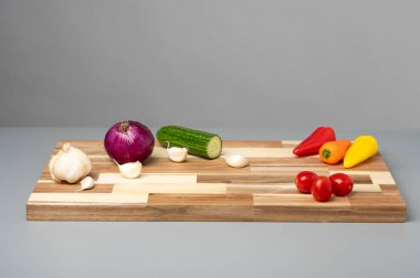 Sarımsaklı, kırmızı soğanlı, salatalıklı, mini dolmalık biberli ve vişneli domatesli tahta bir tahta kesim tahtası..