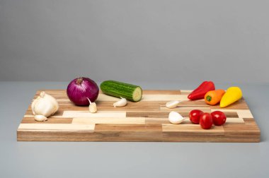 Ahşap kesim tahtasındaki renkli sebzeler gri arka planda.