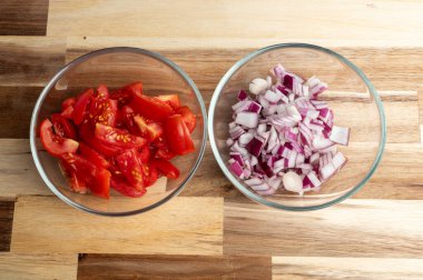 Tahta bir yüzey üzerinde dilimlenmiş domates ve cam kaselerde doğranmış kırmızı soğan.
