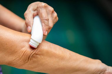 Kıdemli kadının sol el analjezik sıvı kullanarak, kas ağrısı giderici sağ dirsek rulo, mavi yüzme havuzu arka plan, yakın çekim & makro Shot, seçici odak, Asya vücut cilt parçası, Masaj hakkında, sağlık konsepti