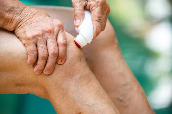 Las manos de la mujer mayor masajeando su rodilla, Usando líquido analgésico, rodillo analgésico para aliviar el dolor muscular en la medicina, Fondo azul de la piscina, Primer plano y Macro shot, Enfoque selectivo, Parte asiática de la piel del cuerpo, Acerca del masaje, Concepto de atención médica — Foto de Stock