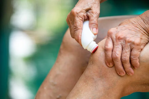 Las manos de la mujer mayor masajeando su rodilla, Usando líquido analgésico, rodillo analgésico para aliviar el dolor muscular en la medicina, Fondo azul de la piscina, Primer plano y Macro shot, Enfoque selectivo, Parte asiática de la piel del cuerpo, Acerca del masaje, Concepto de atención médica — Foto de Stock