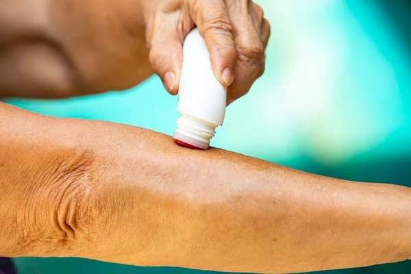 Senior woman's right hand using analgesic liquid, muscle pain reliever roll her left arm, Blue swimming pool background, Close up & Macro shot, Selective focus, Asian Body skin part, About Massage, Healthcare concept