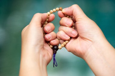 Kadın elleri dua ve bokeh mavi yüzme havuzu arka planda bir boncuk tespih tutarak, Asya vücut dil hissi, namaz Budist, dini konsept
