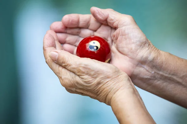 Руки пожилой женщины держат и молятся черно-белый религиозный символ Инь Ян на красном мяче в даосизме на фоне боке синий бассейн, азиатская часть тела кожи, язык тела чувство, религия концепции — стоковое фото