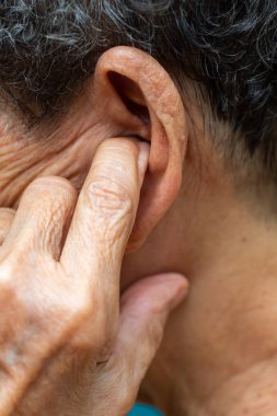Sol kulağına işaret parmağı koyan yaşlı kadın, Gri kıvırcık kıllar, Yüzme havuzu arka planı, Yakın çekim & Makro çekim, Seçici odak, Asya Vücut parçası, Sağlık kavramı, İşitme kaybı belirtisi