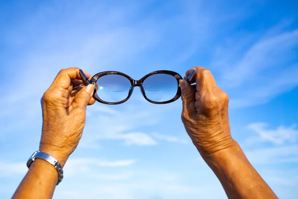 Senior nő kezében szemüveget, hogy a kék ég háttér, ázsiai testbőr rész, Symbol, Geszturing, testbeszéd koncepció, szelektív fókusz — Stock Fotó