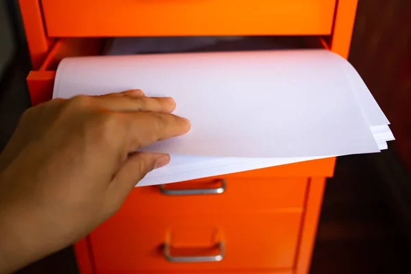 Woman\'s hand pick up white papers for write letter, Filing cabinet with open drawer, Orange metal colour, Administration and storage concept, closeup & Macro shot, Selective focus
