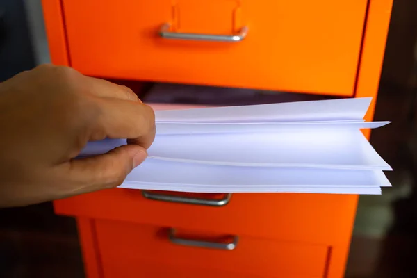 Woman\'s hand pick up white papers for write letter, Filing cabinet with open drawer, Orange metal colour, Administration and storage concept, closeup & Macro shot, Selective focus