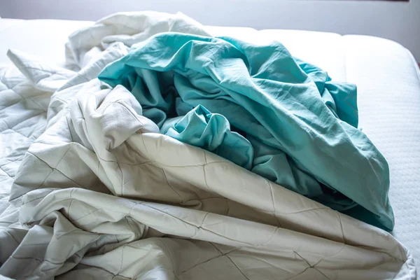 Sábana arrugada turquesa y blanca sobre cama blanca, Primer plano, enfoque selectivo, concepto de limpieza de dormitorios — Foto de Stock