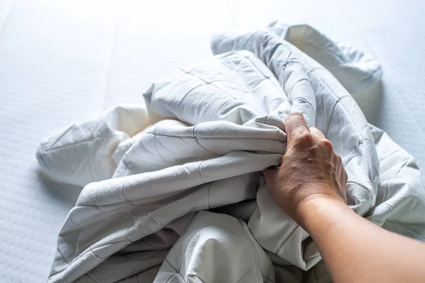 Kvinnans hand plocka upp vita skrynkliga lakan på vit säng, närbild skott, selektiv fokus, sovrum rengöring koncept — Stockfoto