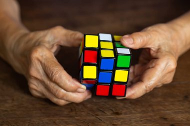 Bangkok, Tayland, 23 Mart 2019, Rubik küpü tutan ve onunla oynayan yaşlı adam, ahşap doku arka plan üzerinde, Rubik küpü Macar mimar Erno Rubik tarafından icat 1974, Close up & Macro çekim, Seçici odak