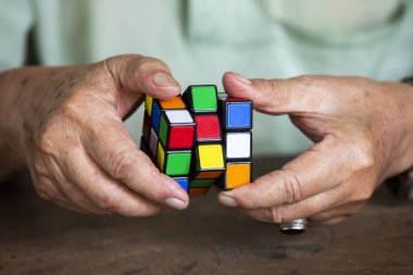 Bangkok, Tayland, 23 Mart 2019, Rubik küpü tutan ve onunla oynayan yaşlı adam, ahşap doku arka plan üzerinde, Rubik küpü Macar mimar Erno Rubik tarafından icat 1974, Close up & Macro çekim, Seçici odak