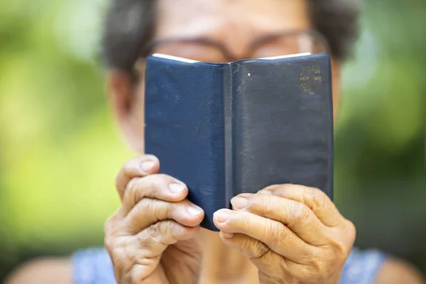 Mujer mayor leyendo un pequeño libro de color azul marino en bokeh gard — Foto de Stock