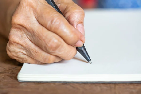 Carta de escritura de mano derecha para mujer mayor sobre fondo de papel marfil, Cuaderno, Un bolígrafo negro, Primer plano y plano macro, Enfoque selectivo, Concepto de papelería — Foto de Stock