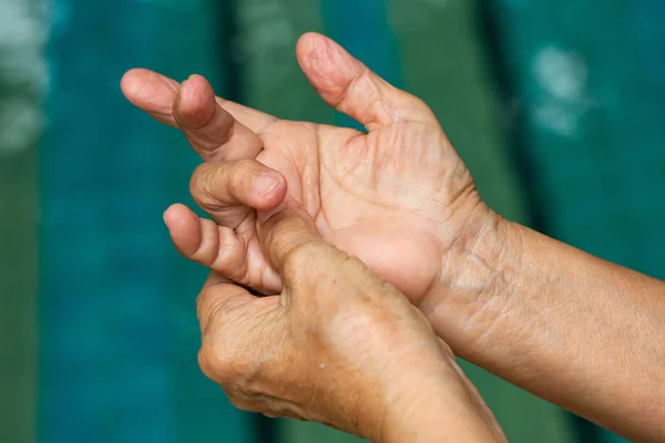 Trigger Finger, Senior woman's left hand massaging her ring finger, Suffering from pain, Close up and macro shot, Swimming pool background, Health care and massage, asian body concept — Stock Photo, Image