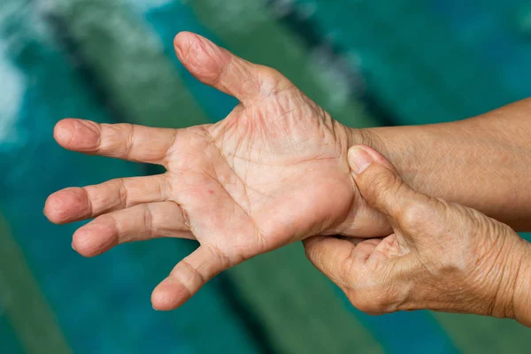 Palec wyzwalacza, Starsza kobieta lewa ręka masując prawą rękę cierpienie z bólu, zbliżenie i makro strzał, basen tło basen, opieka zdrowotna i masaż, koncepcja ciała azjatyckich — Zdjęcie stockowe