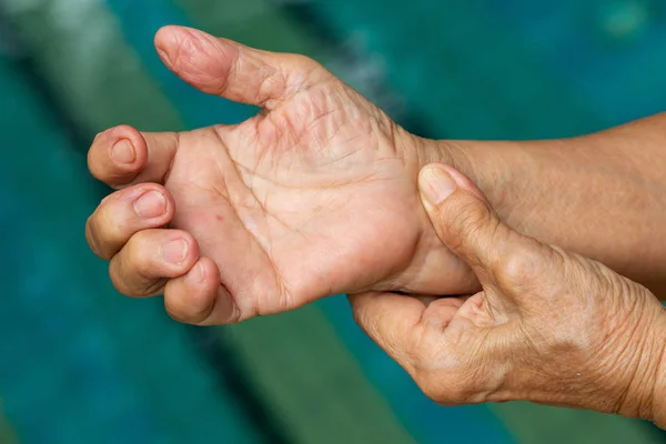 Dedo desencadenante, Mano izquierda de la mujer mayor masajeando su mano derecha Sufriendo de dolor, Primer plano y macro shot, Fondo de la piscina, Cuidado de la salud y masaje, concepto de cuerpo asiático — Foto de Stock