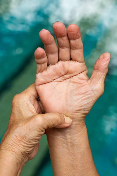 Trigger ujj, Senior nő bal kezét masszírozó jobb keze szenved a fájdalomtól, közelről és makró lövés, uszoda háttér, egészségügyi ellátás és masszázs, ázsiai test fogalma — Stock Fotó