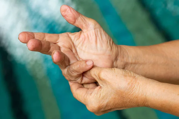 Trigger Finger, Senior woman's left hand massaging her little finger, Suffering from pain, Close up and macro shot, Swimming pool background, Health care and massage, asian body concept — Stock Photo, Image